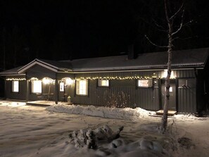 A snow-covered building with a porch, windows, and a tree in the foreground.