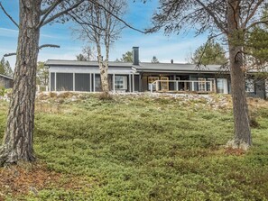 A modern house with a large porch, surrounded by trees and a grassy yard.