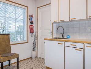 A kitchen with white cabinets, a sink, and a window with blinds.