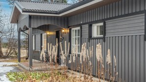 A modern house with a covered porch, a small outdoor seating area, and tall ornamental grasses. - Torvokoski by Interhome (Utsjoki)