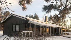 A wooden cabin with a snow-covered roof and a chimney, surrounded by trees and snow. - Torvokoski by Interhome (Utsjoki)