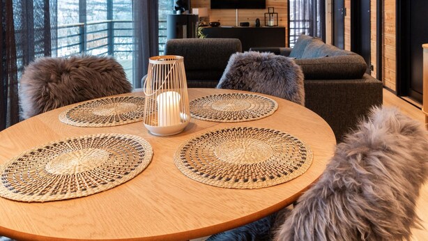 A modern living room with a round wooden table, two fluffy grey sofas, and a TV mounted on the wall. - Saanan lumous by Interhome (Enontekiö)