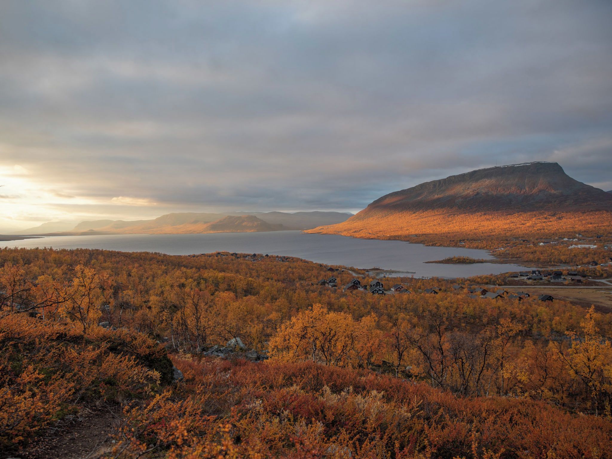 Vuoristoinen maisema, jossa on järvi ja syksyn väreihin muuttuneita puita.