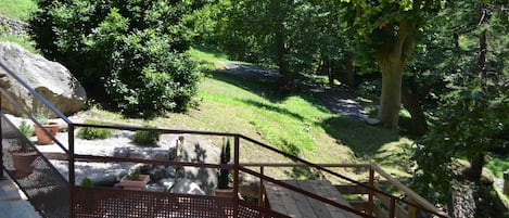 A wooden staircase leading to a garden area with a paved path, surrounded by lush greenery and trees.