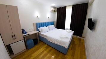 Une chambre d’hôtel équipée d’un lit, d’un bureau, d’une armoire et d’un petit réfrigérateur.