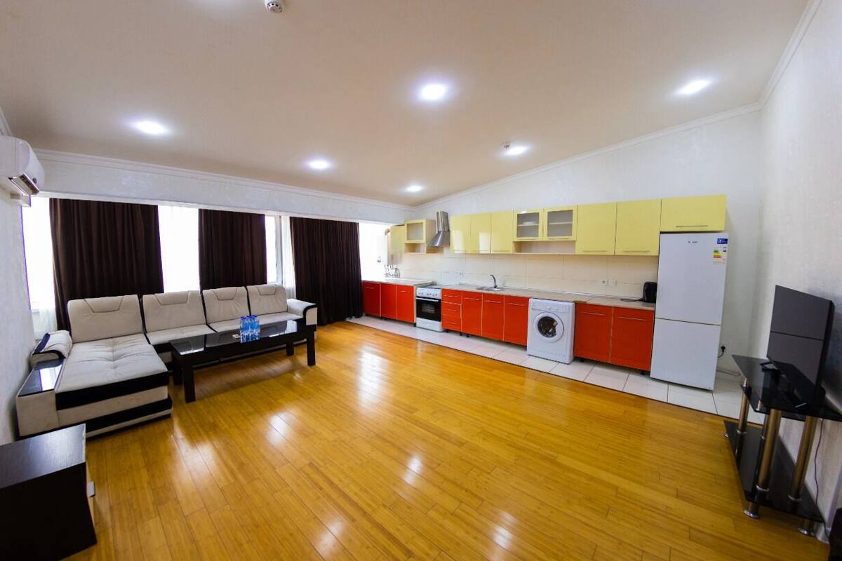 A modern living room with a sofa, coffee table, and a kitchen area with red and white cabinets and appliances.