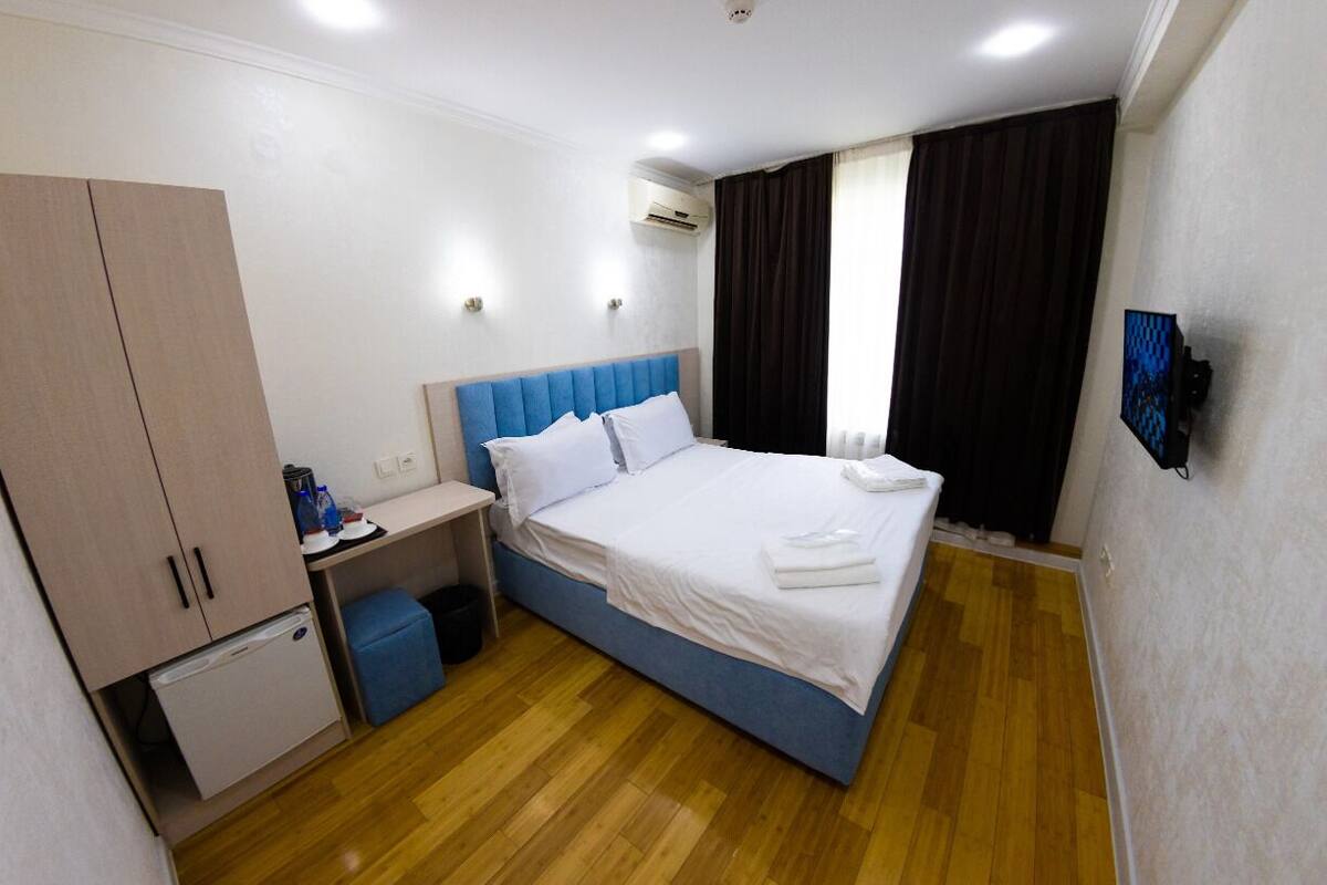 A hotel room with a bed, a desk, a wardrobe, a small fridge, and a TV.