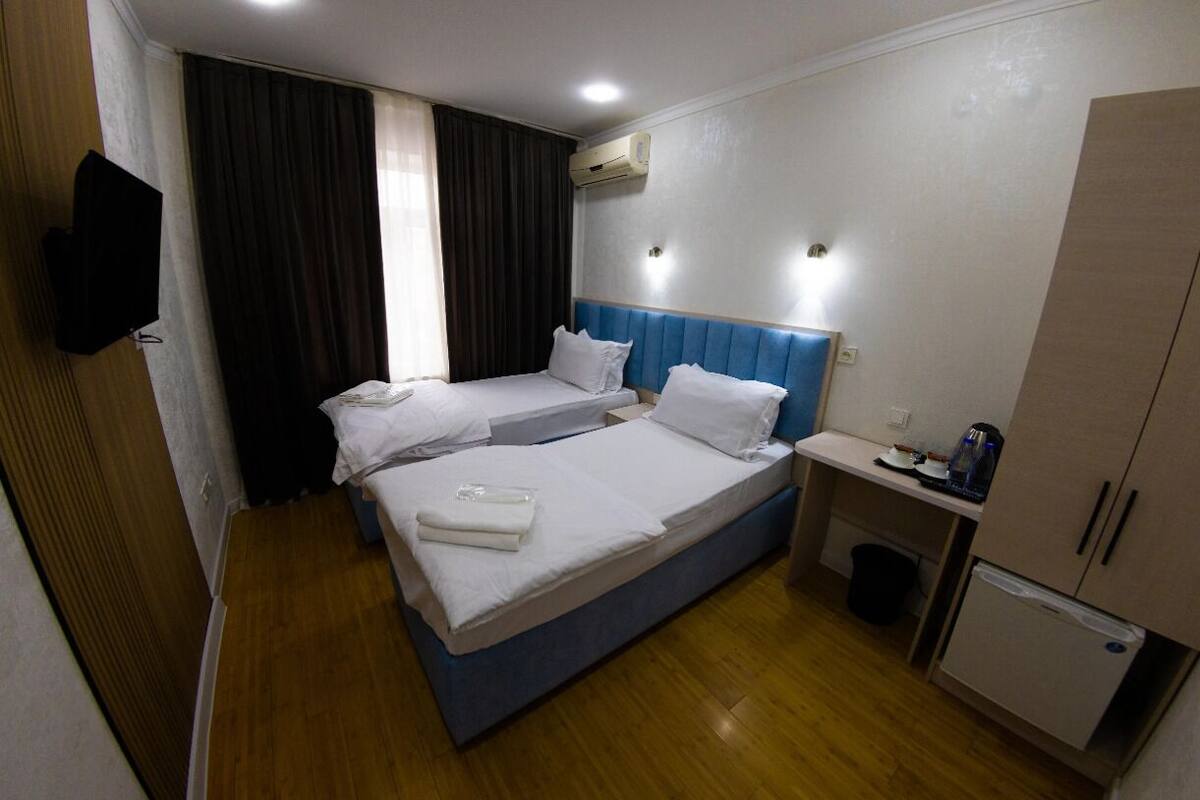 A hotel room with two beds, a small desk, a mini-fridge, and a TV.