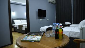 Une chambre d’hôtel avec un lit, un téléviseur fixé au mur, une table avec un magazine, des verres et des bouteilles d’eau et de jus de fruits.