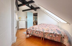 Une chambre avec un plafond en pente, un lit recouvert d’une couvre-lit à motifs floraux, une commode et une chaise.