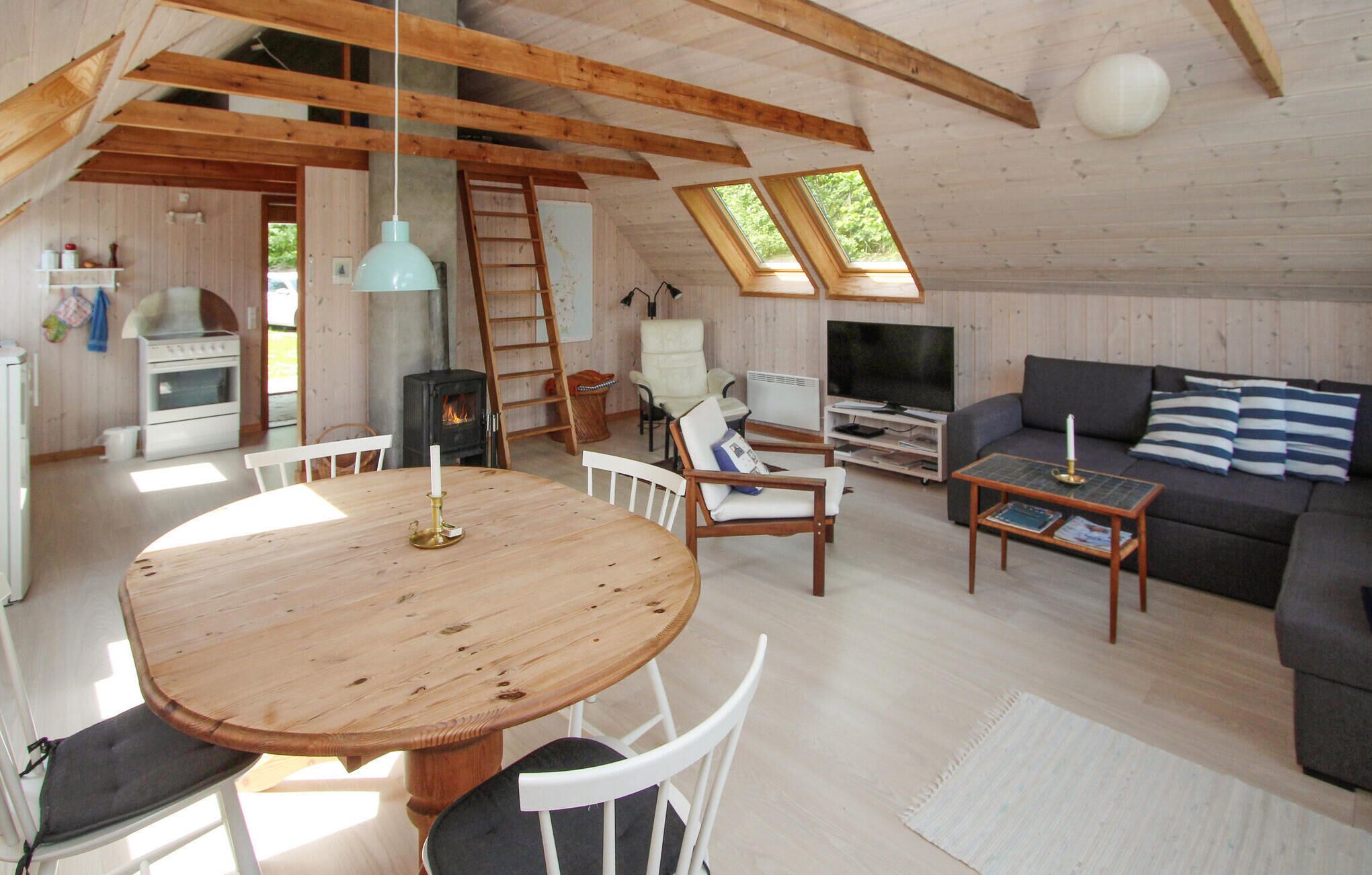 Ein gemütliches Blockhaushaus-Interieur mit einem Holzespeisetisch, weißen Stühlen, einem grauen Sofa, einem Fernseher und einem Kamin.
