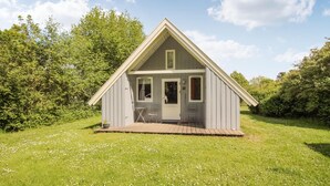 En liten, envåningsstuga med ett sadeltak, en veranda och en dörr med ett fönster.