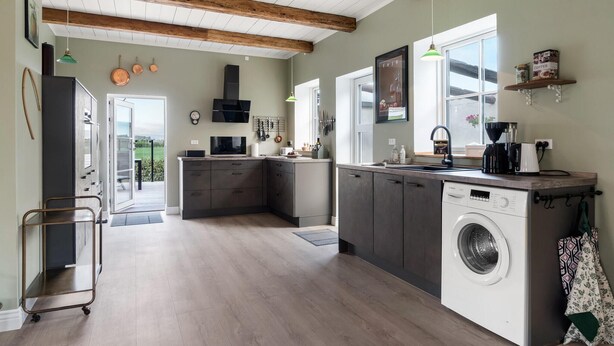 A modern kitchen with wooden beams, a washing machine, and a coffee maker. - Lovely home in Fejø with WiFi (Fejø)