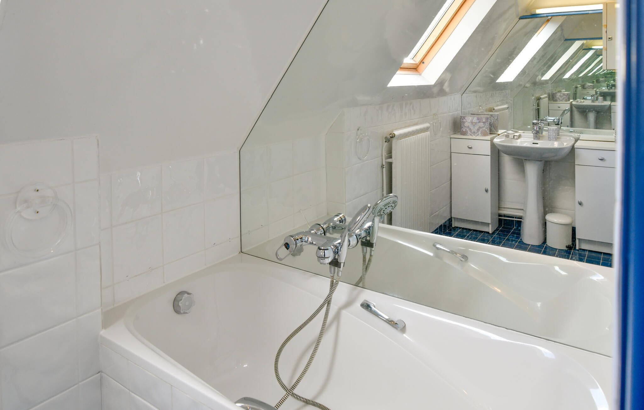 A modern bathroom with a freestanding bathtub, a showerhead, and a mirror reflecting a sink and cabinet.