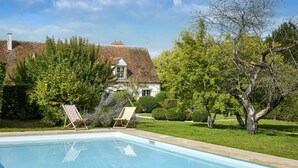 A swimming pool with two lounge chairs, a white house with a red-tiled roof, and a well-maintained garden with trees and shrubs. - Lovely home in Yèvre-la-Ville (Yèvre-la-Ville)