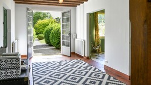 A hallway with a patterned rug, wooden ceiling beams, and a view of a garden through open doors. - Lovely home in Yèvre-la-Ville (Yèvre-la-Ville)