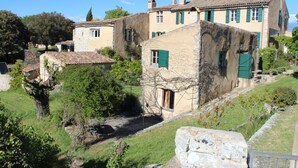 A traditional stone building with a sloped roof, green shutters, and a stone staircase leading to the entrance.
