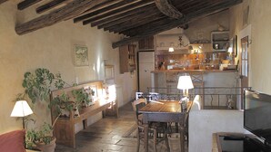 A rustic kitchen with wooden beams, a dining table, and a television.