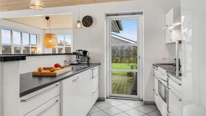 Eine moderne Küche mit weißen Schränken, einer schwarzen Arbeitsplatte und einem großen Fenster mit Blick auf einen Garten.