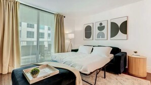 A modern bedroom with a large bed, a side table, and a view of a building through a window.