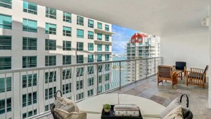 A balcony with wicker furniture, a small table with a tray, and a view of a modern building with many windows.