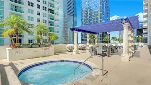 A rooftop pool with a blue-tiled edge, surrounded by palm trees and a covered seating area.