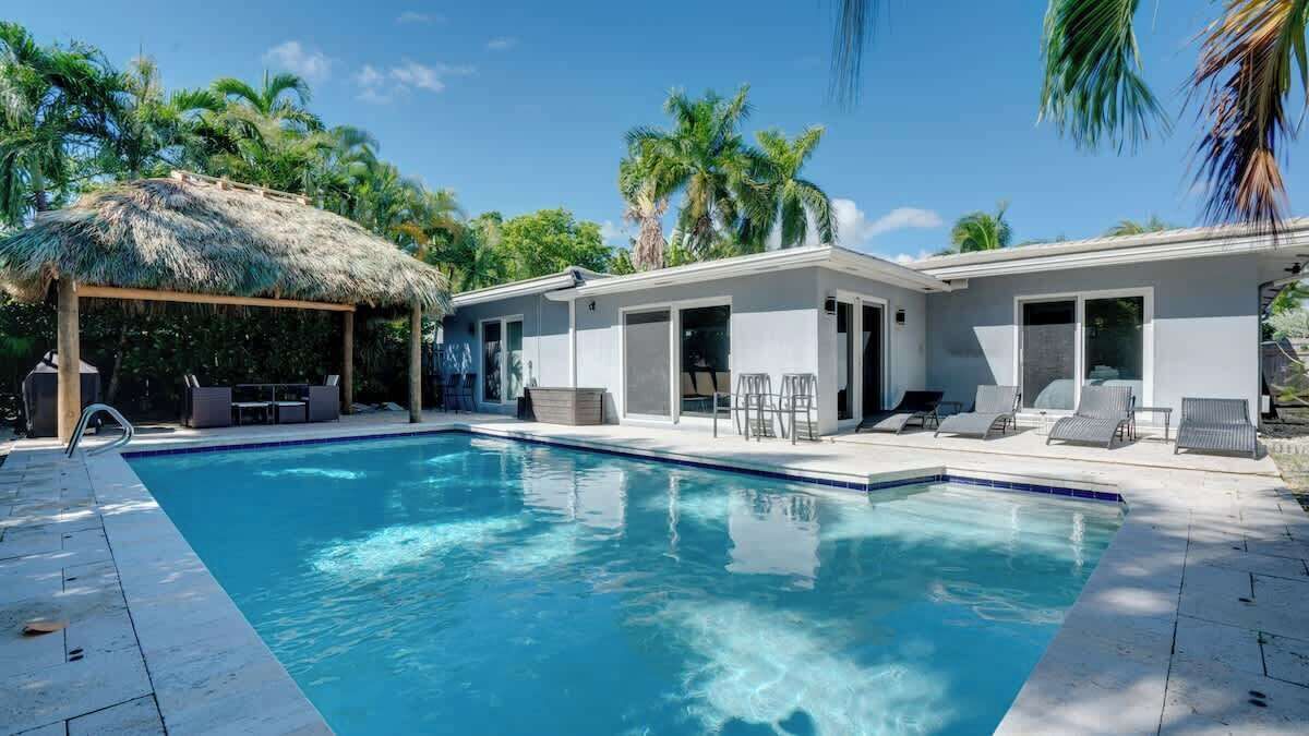 A modern pool area with a thatched roof structure, lounge chairs, and a clear blue pool.