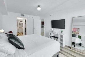 Ein modernes Schlafzimmer mit einem großen Bett, einem Flachbildfernseher, einem Kleiderschrank und einem Spiegel.