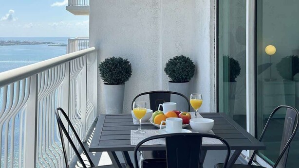 Un balcon avec une table dressée pour le petit-déjeuner, deux plantes en pot et une vue sur la mer.
