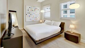 Een moderne hotelkamer met een groot bed, een flatscreen televisie, een kunstwerk aan de muur en een raam dat natuurlijk licht binnenlaat.