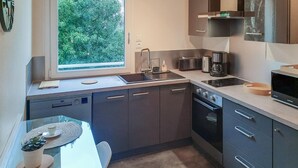 A modern kitchen with a built-in dishwasher, a microwave, and a stove. There is a window providing natural light and a view of greenery outside. - Nice apartment in Redon with WiFi (Redon)