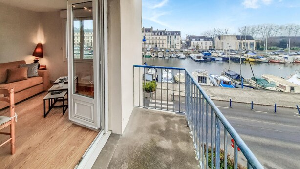 A balcony with a sofa, a table, and a lamp. It overlooks a marina with boats and buildings. - Nice apartment in Redon with WiFi (Redon)