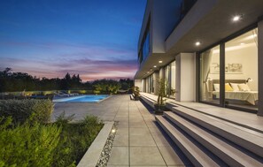 A modern building with a swimming pool, outdoor seating, and a well-lit interior. - Awesome home in Rakalj (Rakalj)