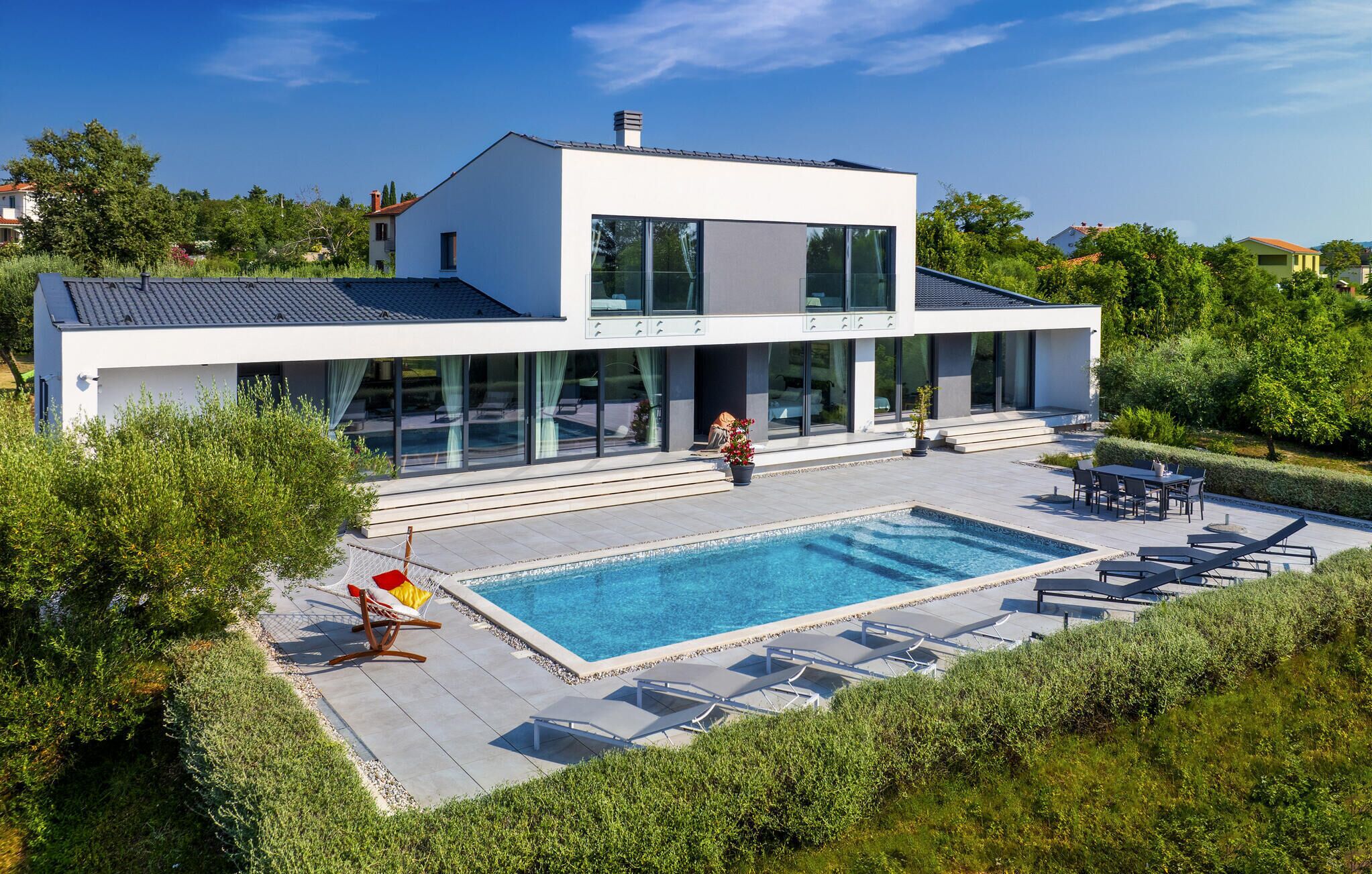 Una casa moderna de dos pisos con piscina, mobiliario exterior y un jardín cuidado.