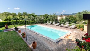 Une piscine entourée de chaises longues, de pots en terre cuite, et offrant une vue sur la campagne.