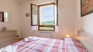 Une chambre à coucher avec un lit, une commode, une fenêtre donnant sur un paysage verdoyant et un tableau accroché au mur.