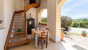 Une cuisine avec un escalier en bois, une table à manger avec des chaises, un poêle à bois encastré et une vue sur l’extérieur.