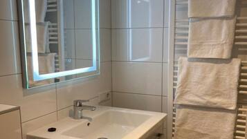 Un baño con un lavamanos blanco, un espejo con luz y un perchero con toallas.
