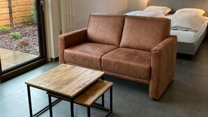 A modern room with a brown leather sofa, a wooden coffee table, and a bed with white bedding. - Appartement Ellemeet (Ellemeet)