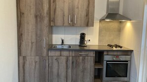 A compact kitchen with wooden cabinets, a stainless steel range hood, a built-in oven, and a sink. - Appartement Ellemeet (Ellemeet)