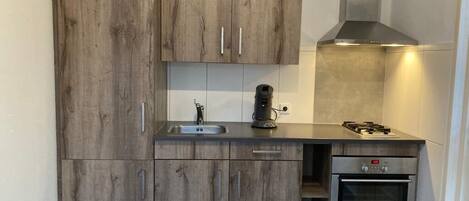 Une cuisine compacte dotée de meubles en bois, d’une hotte en acier inoxydable, d’un four encastré et d’un évier.