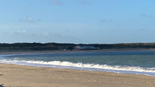 A beach with waves, a pier, and a building in the background. - Appartement Ellemeet (Ellemeet)