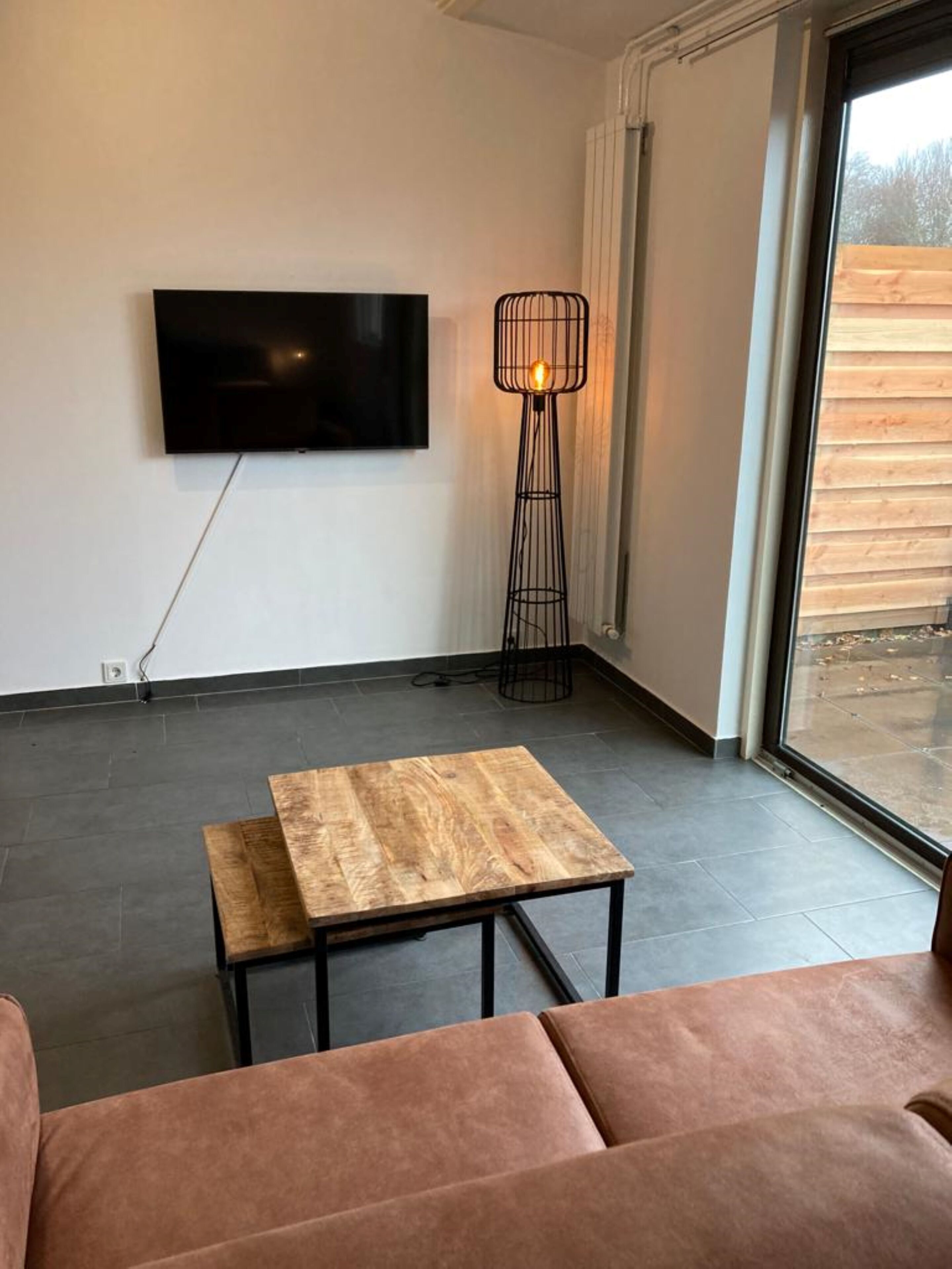 Un salon moderne avec un téléviseur à écran plat fixé au mur, un grand lampadaire et une table basse en bois.