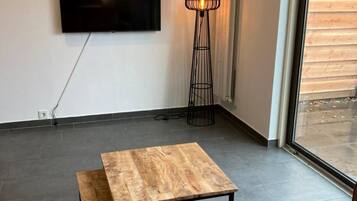 Un salon moderne avec un téléviseur à écran plat fixé au mur, un grand lampadaire et une table basse en bois.