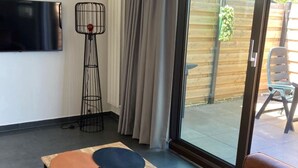 A modern living room with a sofa, a small table, a floor lamp, and a sliding glass door leading to an outdoor area. - Appartement Ellemeet (Ellemeet)