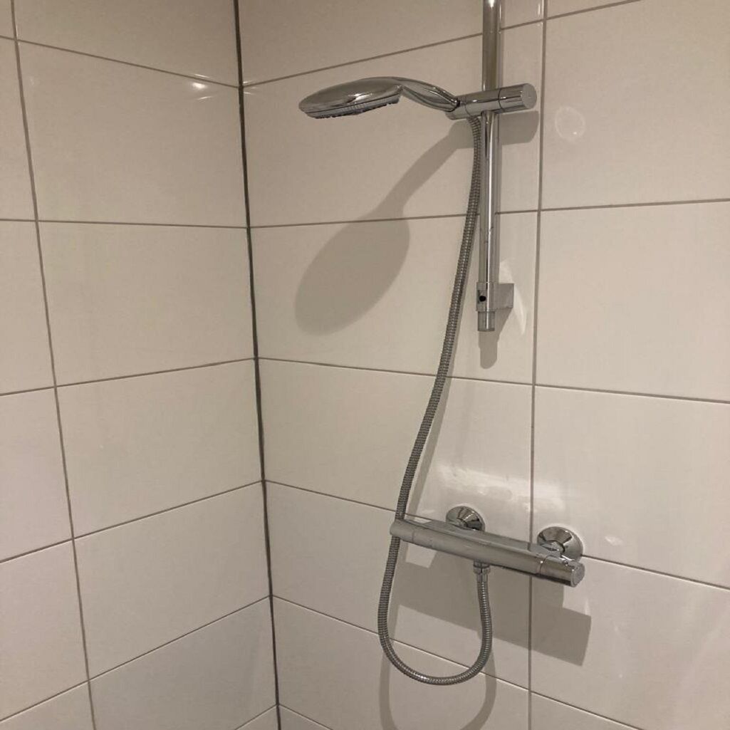 A shower with a handheld showerhead and a handheld hose, mounted on a tiled wall.