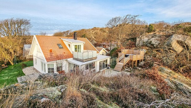 Une maison moderne avec un toit en pente, une véranda en verre et une terrasse en bois.