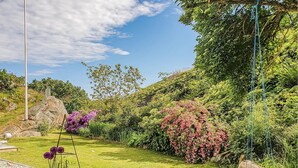 Un jardin avec une balançoire, une balançoire en bois et une variété d’arbustes à fleurs.