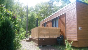 A wooden cabin with a deck, surrounded by dense greenery. - Tiny house in unspoiled nature on Lake Plau (Bad Stuer)