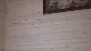 A bedroom with a wooden wall, a bed with grey bedding, and a painting above the bed. - Tiny house in unspoiled nature on Lake Plau (Bad Stuer)